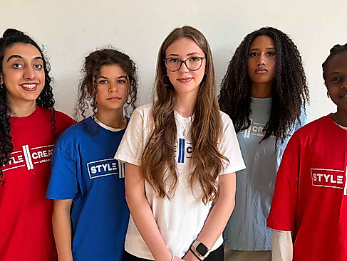 Fünf Personen mit unterschiedlichen Haarlängen und -strukturen tragen bunte T-Shirts mit dem Schriftzug "STYLE CREATE" und stehen vor einer hellen Wand.