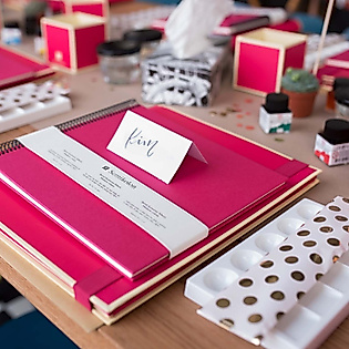 Vorbereiteter Lettering-Workshop-Tisch mit roten Mappen, Namensschildern, Tinte und Kreativmaterialien
