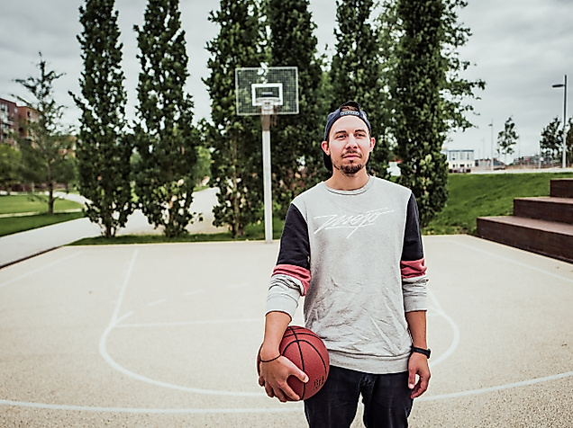 Junger Mann mit Basketball steht auf dem Sportfeld im Lohsepark vor einem Korb und hohen Bäumen
