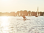 Person paddelt im Kanu auf der Alster bei Sonnenuntergang, umgeben von zahlreichen Segelbooten