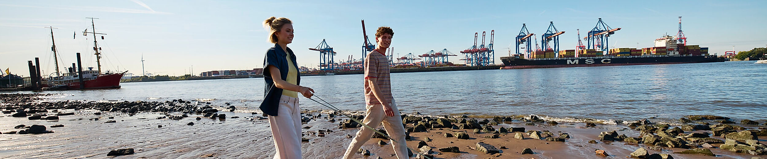 Ein junges Paar geht mit Hund an der Elbe spazieren.
