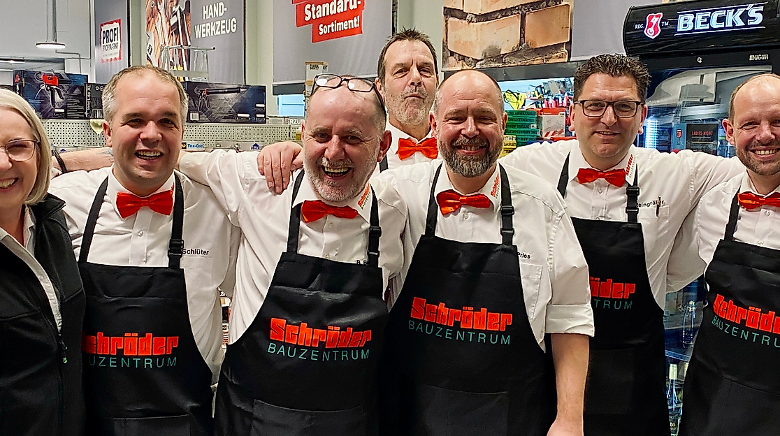 Man sieht die Kolleginnen und Kollegen, die für euch am Abend der Ladies Night 2025 im Schröder Bauzentrum in Itzehoe, die Getränkte ausgeteilt haben. Mit einem weißen Hemd, roter Schleife und einer schwarzen Schröder-Schürze stehen sie auch dieses Jahr wieder bereit und freuen sich auf euch!