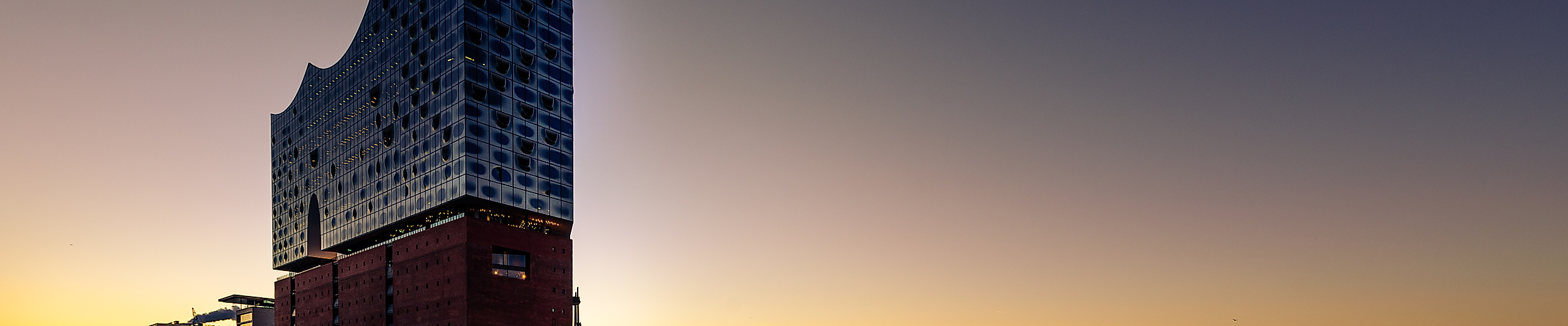 Elbphilharmonie von unten bei Sonnenuntergang mit Hafenblick