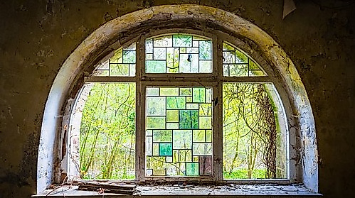 Blick aus einem Rundbogenfenster, mit Bleikristalleinfassungen im Grünton, in die Natur