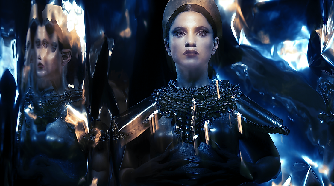Surrounded by mirrored surfaces, the made-up head of a person can be seen wearing a headpiece and reflective costume.