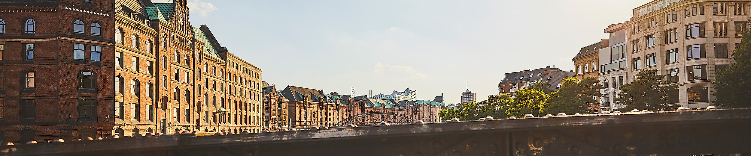 Blick über eine Brücke auf die Fleete und Backsteinfassaden der Speicherstadt bei tief stehender Sonne