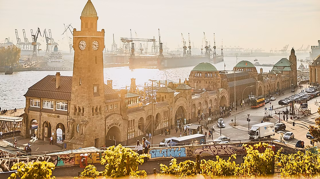 Uhrturm und Gebäude der Landungsbrücken im warmen Licht der Abendsonne mit Blick auf Elbe und Kräne