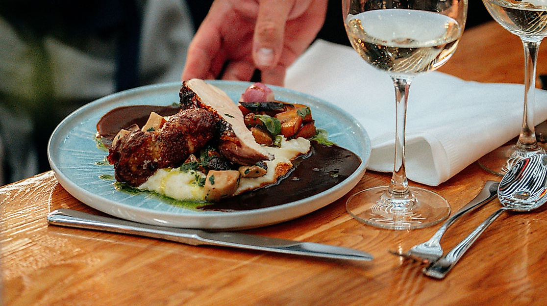 Fein angerichtetes Hauptgericht mit Gemüse und Fleisch beim OPEN MOUTH Food Festival, serviert mit Weißwein.