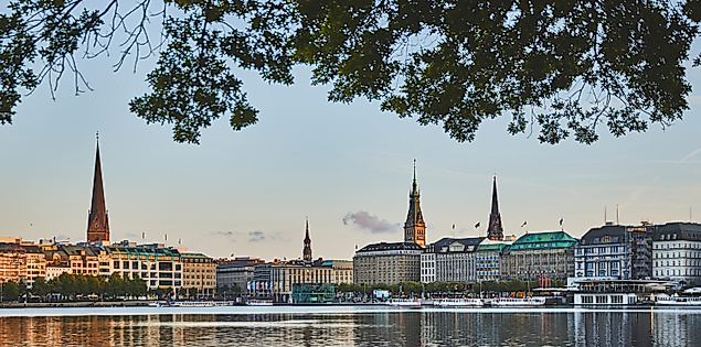 Binnenalster, im Hintergrund Jungfernstieg und Hamburger Altstadt mit Rathaus und Kirchtürmen bei Abenddämmerung.