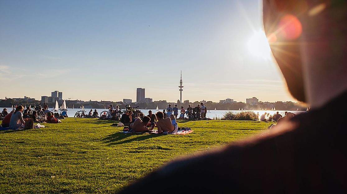 Menschen entspannen im Alsterpark bei Sonnenschein mit Blick auf die Außenalster und die Skyline Hamburgs