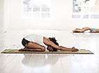 Person praktiziert Yoga in der Kindhaltung auf Matte in hellem Raum mit Holzfußboden