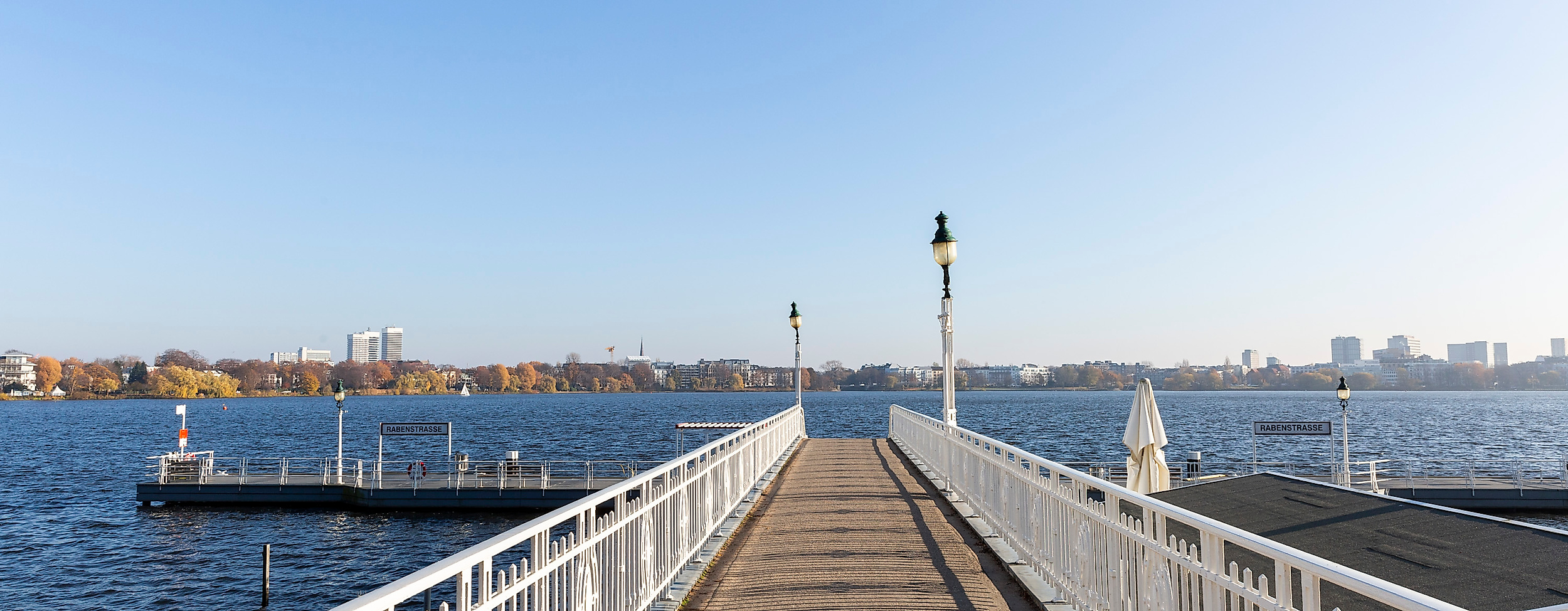 Steg an der Außenalster in Hamburg mit weitem Blick über das Wasser und die Skyline bei strahlend blauem Himmel