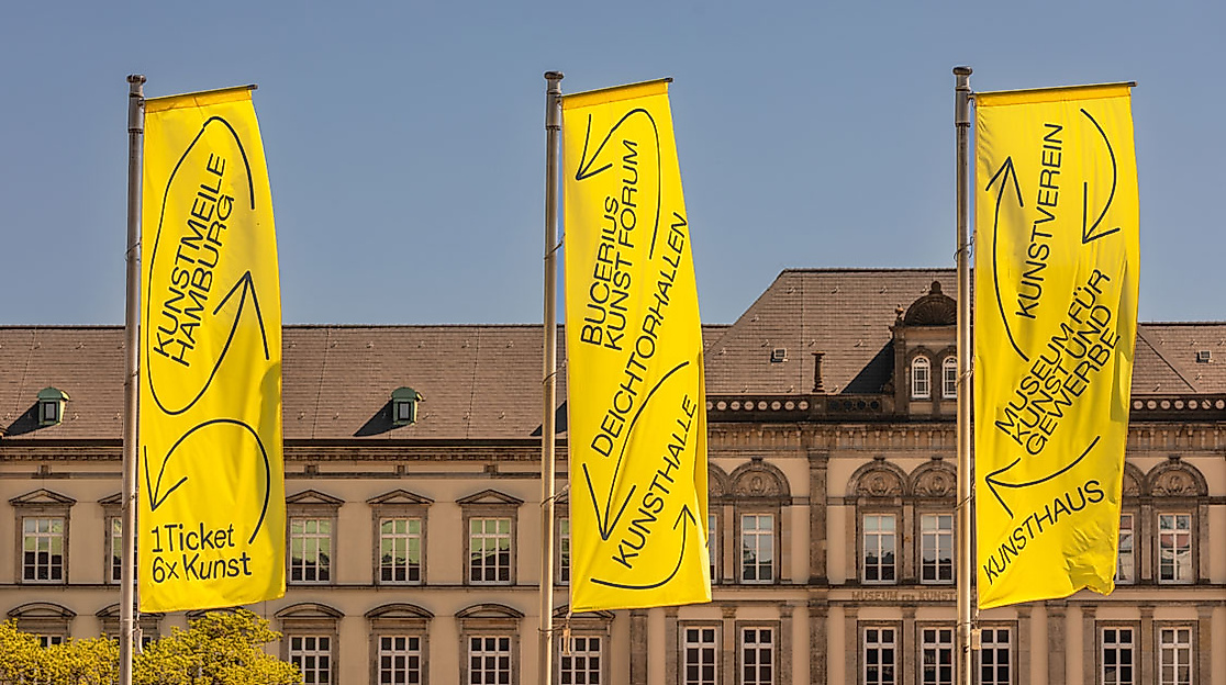 Gelbe Kunstmeile-Fahnen vor klassizistischer Fassade am Hamburger Glockengießerwall bei blauem Himmel