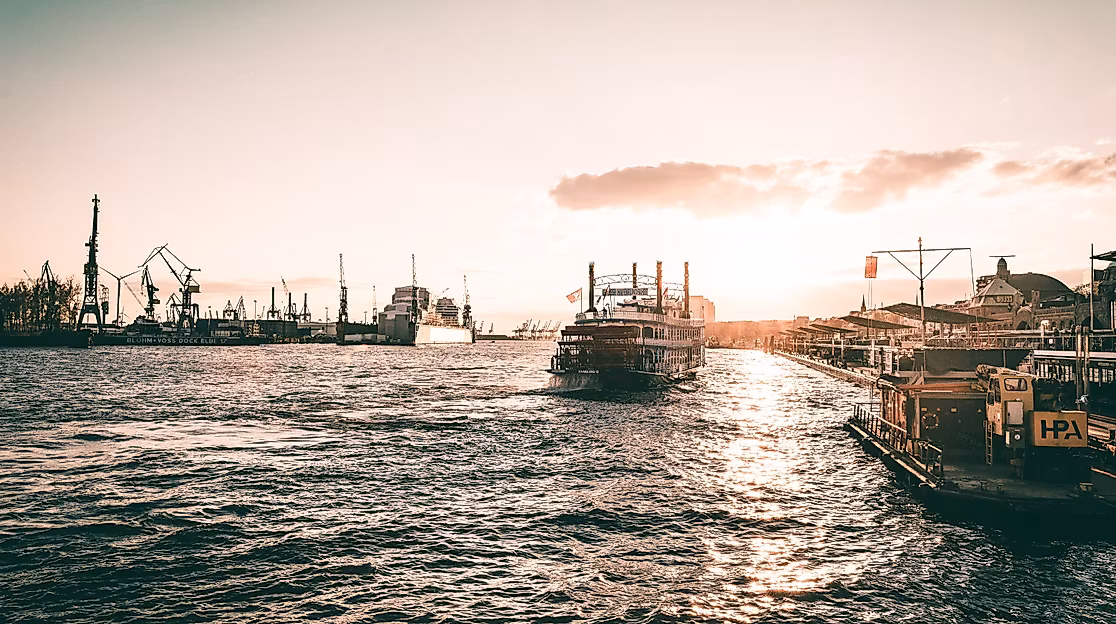 Boote auf der Elbe im Hamburger Hafen bei Sonnenuntergang mit glitzerndem Wasser und Hafenkränen