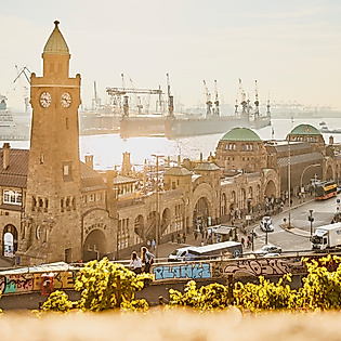 Uhrturm und Gebäude der Landungsbrücken im warmen Licht der Abendsonne mit Blick auf Elbe und Kräne