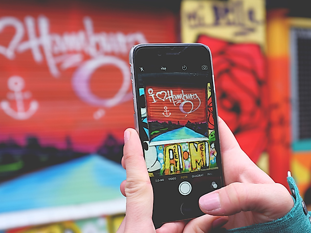 Smartphone fotografiert buntes Hamburg-Graffiti, Symbol für Social Media und Influencer-Kommunikation