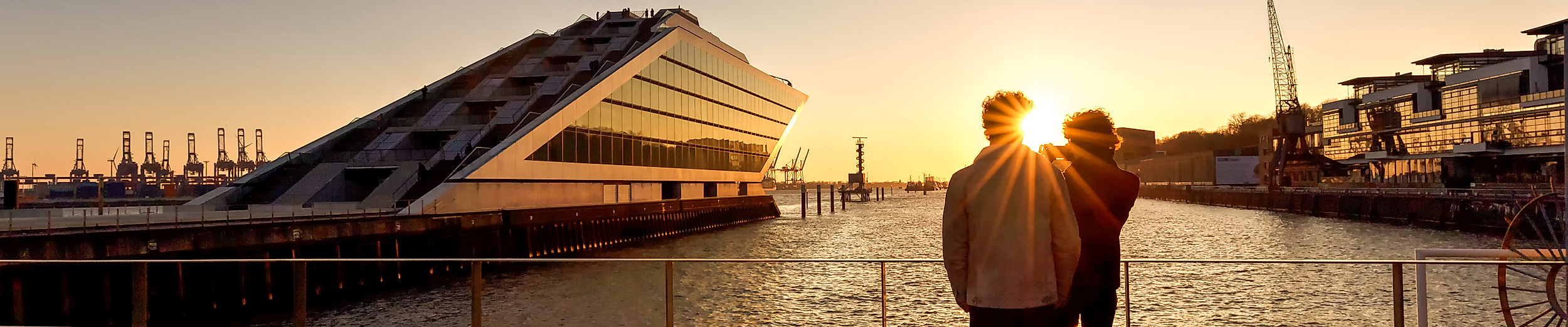 Zwei Menschen fotografieren den Sonnenuntergang am Hafen