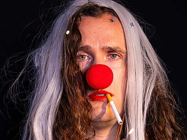 A person in a clown costume has a cigarette in their mouth. The cigarette is lit.