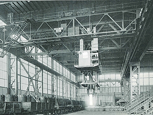 An old black and white photo of the former factory buildings of Kampnagel with scaffolding, a crane and metal barrels lined up.