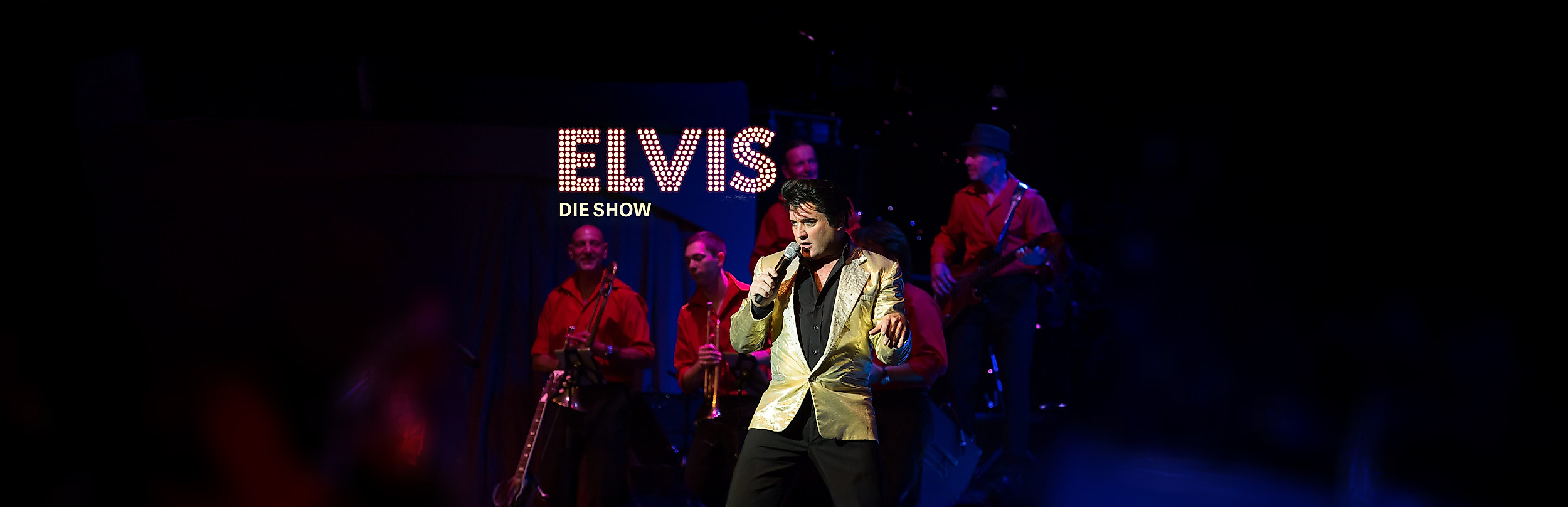 Elvis Darsteller auf der Bühne mit Band im Hintergrund