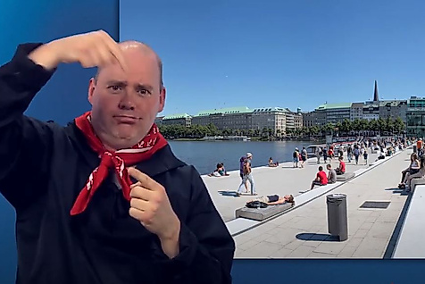 Mann gebärdet vor sonniger Alsterpromenade mit vielen Menschen – barrierefreie Informationen zur Alster in Hamburg.