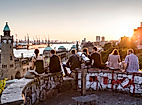 Menschen sitzen bei Sonnenuntergang oberhalb der Landungsbrücken mit Blick auf Hafen und Elbe