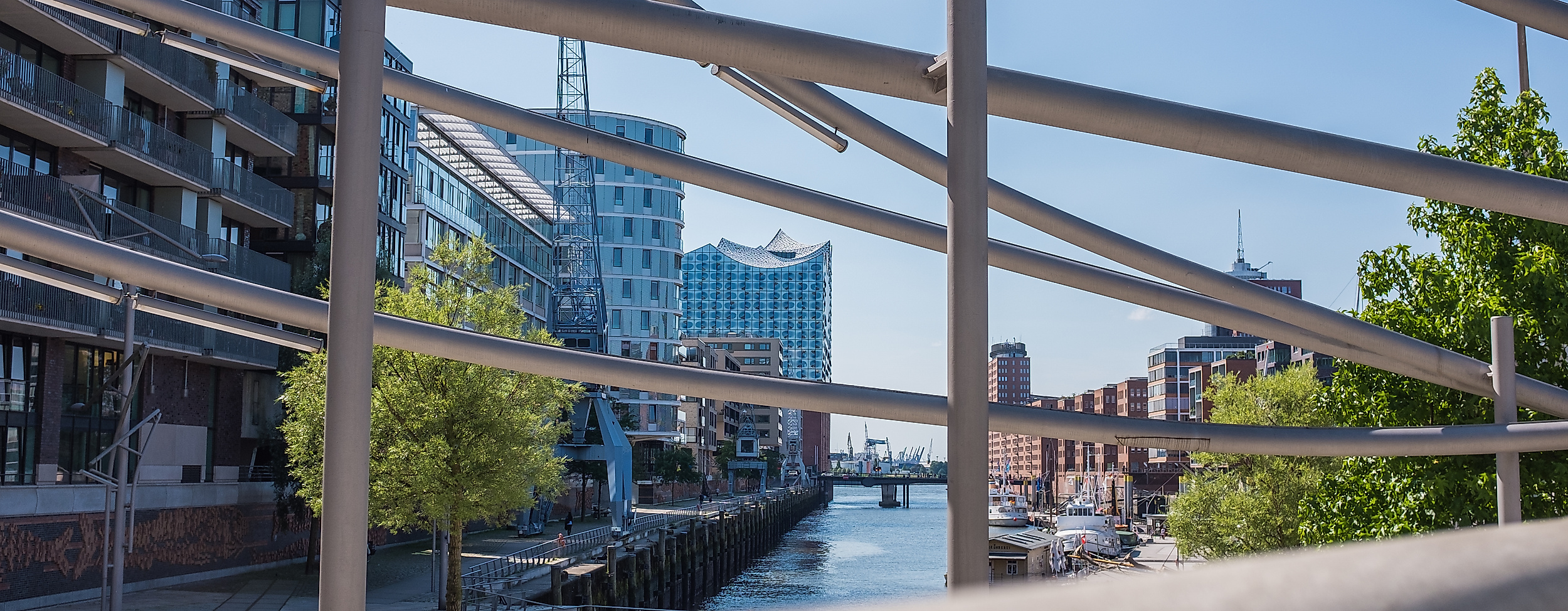 Blick durch Geländer auf Fleet in der HafenCity Hamburg mit moderner Architektur und blauem Himmel